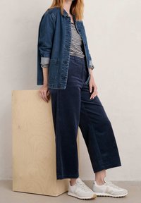 Jeansjacka, randig topp och vida kordbyxor i marinblå; kombinerat med ljusa sneakers. Detaljer inkluderar knappar och uppvikta ärmar.