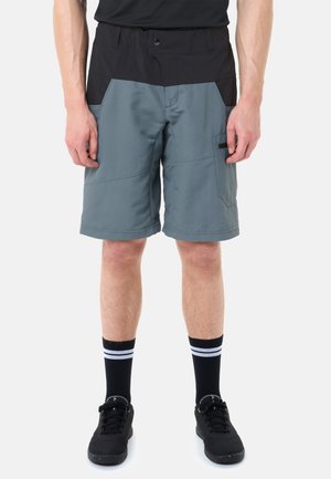 Mann trägt zweifarbige schwarze und graue knielange Shorts, schwarze Sportschuhe und schwarze Socken mit weißen Streifen, steht vor einem weißen Hintergrund.