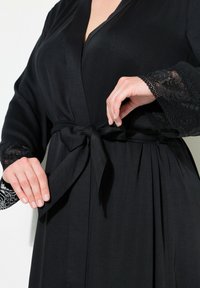 Černý župan s pásem v pase, vyznačující se krajkovými detaily na rukávech a volným střihem. Hladká textura a elegantní splývání.