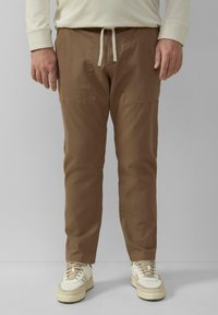 Bruine katoenen cargobroek met voorzakken, een trekkoord tailleband en taps toelopende pijpen, gecombineerd met witte en beige sneakers.