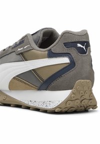 Graue, beige und marineblaue Puma-Sneaker-Ferse mit weißem Schriftzug, strukturiertem Sohlenbereich mit kreisförmigen Griffmustern und gepolstertem Schaftrand.