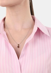 Collarín de camisa a rayas rosas con un collar de cadena de plata que lleva dos piedras ámbar: una en forma redonda y otra en forma de corazón.