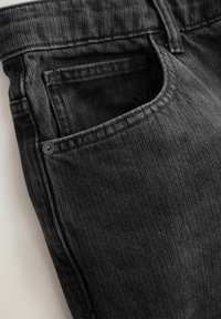 Černé džínsy z denimu s texturovaným vzorem, viditelným prošíváním kapes a kovovým akcentem na kapse. Detailní pohled na oblast pasu.