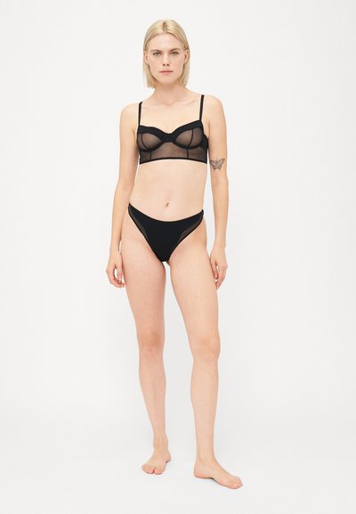 Zwarte mesh lingerie set bestaande uit een balconette bh met beugel en bijpassende string. Minimalistisch ontwerp met verstelbare bandjes en transparante textuur.