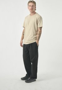 Beige Baumwoll-T-Shirt mit kurzen Ärmeln, Rundhalsausschnitt, lockerer Passform, kombiniert mit schwarzen lässigen Hosen und dunklen Sneakern. Minimalistisches Design.
