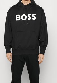 Black hoodie made from soft fabric, featuring a front pocket, drawstring hood, and large white "BOSS" logo across the chest.