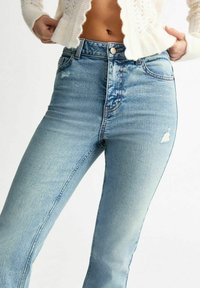 Jeans de mezclilla azul claro con una cintura alta, que presentan un aspecto deslavado y un ligero desgaste. Diseño clásico de cinco bolsillos con un botón plateado.