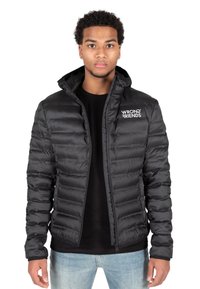 Puffy schwarze Jacke mit einem Reißverschluss vorne und Kapuze, mit vertikalen Nähten und einem weißen Logo auf der linken Brust. Tragen über einem schwarzen Shirt.