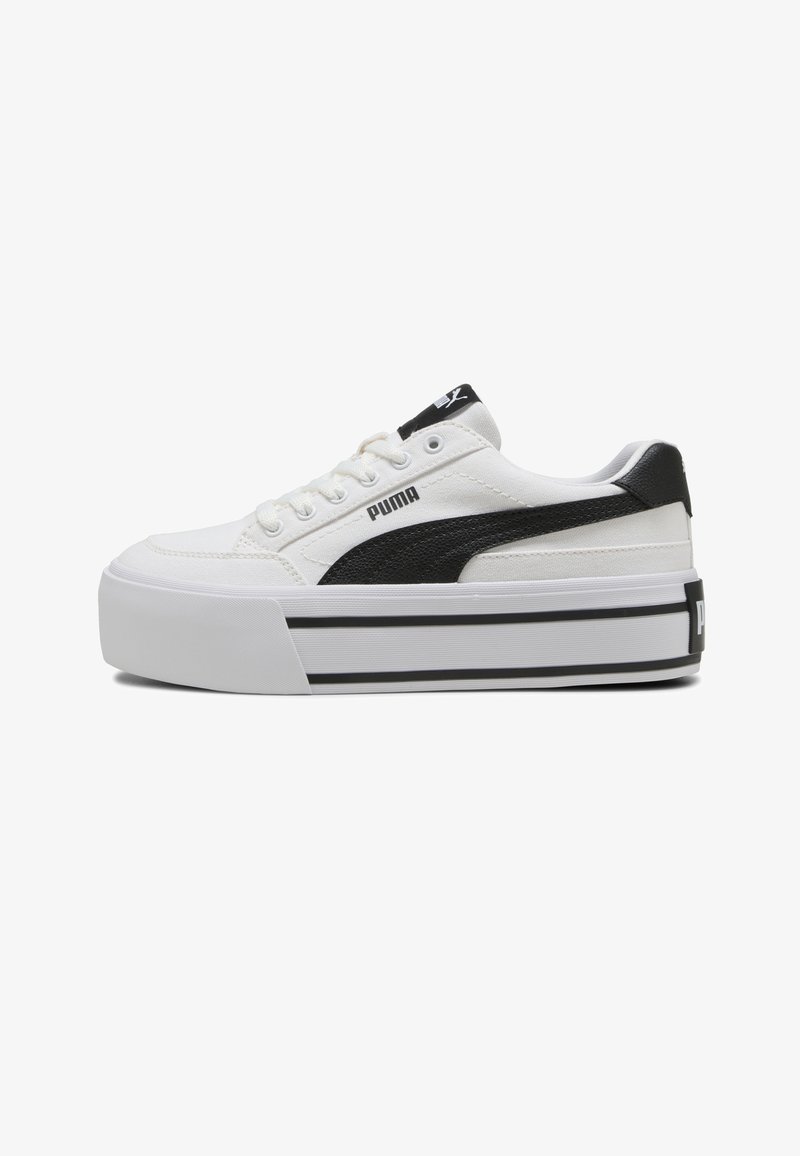 Baskets blanches Puma avec semelle plateforme épaisse, bande noire Puma sur le côté, patch noir au talon et lacets blancs sur fond blanc.