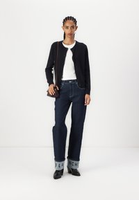 Navy knit cardigan, white ribbed top, dark denim wide-leg jeans with light cuff, black heeled shoes, small brown crossbody bag.
