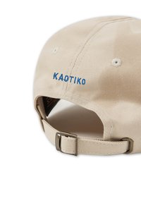 Gorra de béisbol de algodón beige con el logo "KAOTIKO" bordado en azul. Correa ajustable con hebilla de metal; textura suave y diseño de copa redonda.