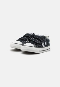 Sorte lerret sneakers med hvite gummisåler, med to borrelåser, stikningsdetaljer og en stjernedetalj på siden.