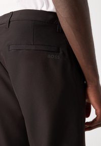 Black trousers with a smooth texture, featuring a back pocket and a subtle BOSS logo in grey. Modern cut, minimalistic design.