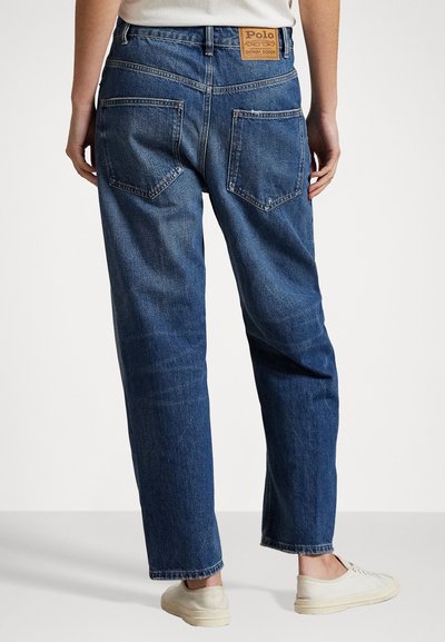 Blue denim jeans with a relaxed fit, straight legs, visible seam details, and two back pockets. A brown leather tag is attached at the waist.