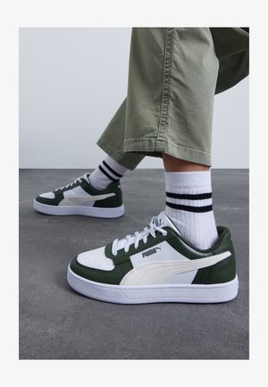 Baskets vertes et blanches avec tige en cuir, bout perforé et semelle en caoutchouc. Présente un système de laçage et des chaussettes rayées.