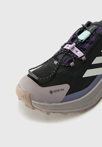 Chaussures de trail GORE-TEX noires avec accents violets, dotées d'un dessus texturé, d'une semelle robuste et d'un système de laçage innovant pour un fit sécurisé.