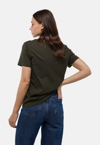 T-shirt en coton vert olive avec un col rond et des manches courtes, associé à un jean bleu taille haute. Design simple et ajusté.