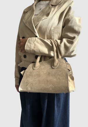 Borsa in suede beige con due manici, design strutturato e base piatta, caratterizzata da cuciture sottili e dettagli arrotondati.