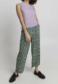 Lila ärmlös topp med volangaxlar, i kombination med gröna blommiga vida byxor. Svarta loafers kompletterar looken.