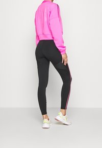 Leggings neri a vita alta con strisce laterali rosa, abbinate a una felpa cropped di un vivace rosa, con polsini a coste e una vestibilità rilassata.