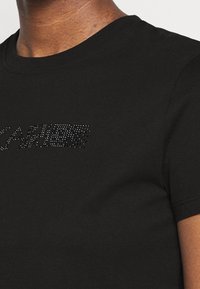 Černé tričko s krátkým rukávem vyrobené z bavlny, s kulatým výstřihem a krystalovými ozdobami, které tvoří slovo "KARL" na přední straně.