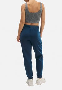 Top corto gris y pantalones jogger navy con cinturilla elástica, vistos desde atrás, combinados con zapatillas blancas.