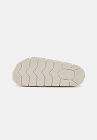 Semelle de sneaker en caoutchouc blanc présentant un motif de crantage en zigzag, des accents texturés et une légère courbure au niveau des orteils pour une meilleure adhérence.