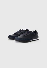 Sötétkék sneaker, sima bőr felső résszel és velúr díszítéssel. Gumitalppal és klasszikus fűzős kivitelezéssel rendelkezik.