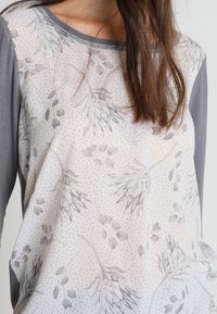 Graues Langarmoberteil mit einer hellen, floralen Musterung auf der Vorderseite und einer gepunkteten Textur. Weiches Material mit kontrastierenden Ärmeln. Schlichter Halsausschnitt.