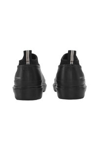 Zapatos de goma negra con acabado liso, puntera redondeada, suela texturizada y lengüetas dobles de colores en el talón.