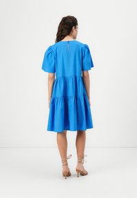Blue cotton dress with puff sleeves and a tiered skirt. Keyhole back detail, smooth texture. Footwear features strappy ankle ties.
