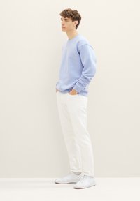 Felpa azzurra chiara con collo rotondo, maniche lunghe e testo bianco; abbinata a pantaloni bianchi e scarpe sportive chiare. Design semplice e moderno.