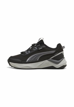 Schwarzer und grauer Puma Low-Top-Sneaker mit dicker weißer Sohle, reflektierenden Details und Kordelverschluss mit Stopper, seitlich vor weißem Hintergrund abgebildet.