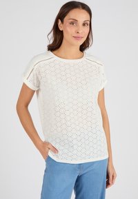Top blanco de manga corta con tejido perforado, escote redondo y puños enrollados. Combinado con jeans de color azul claro. Textura suave, ajuste casual.