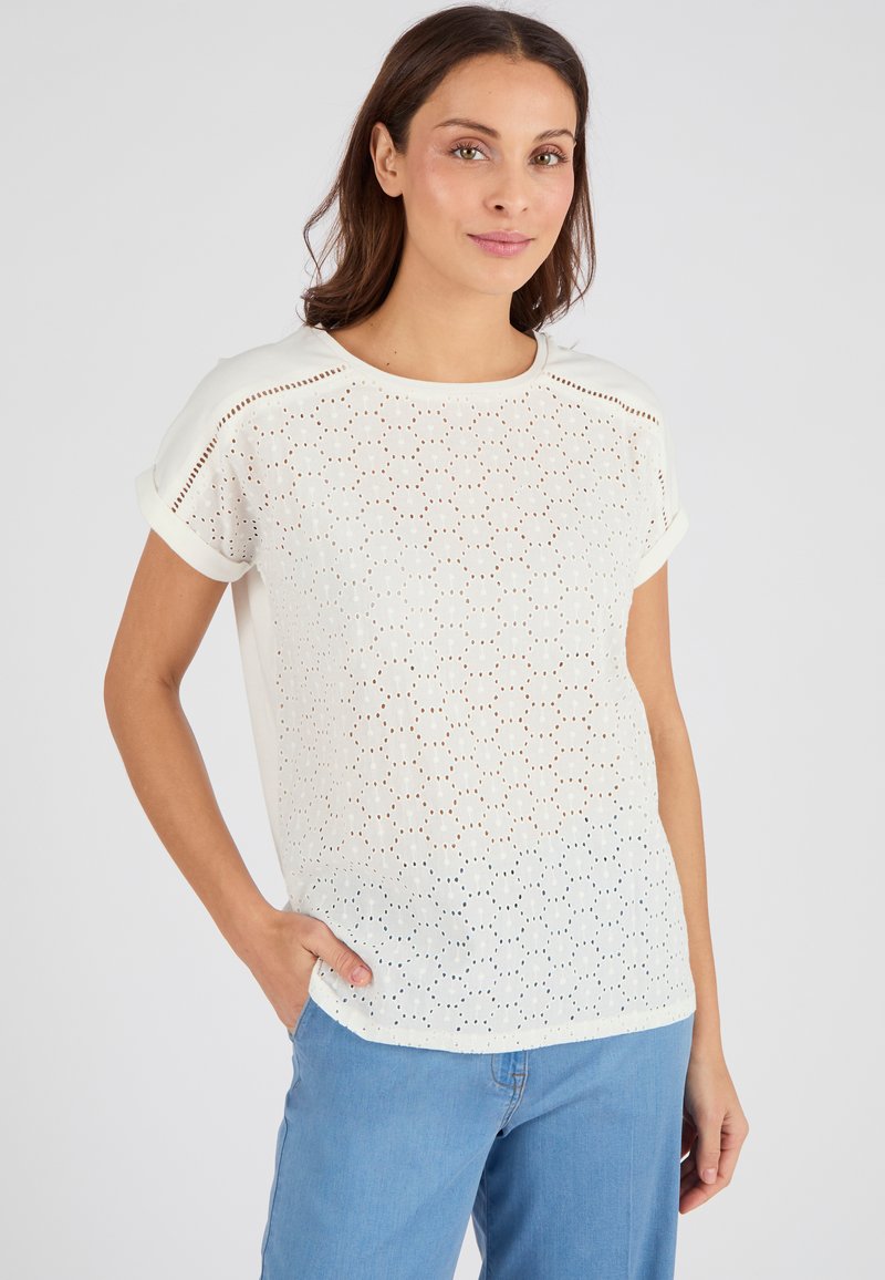 Witte top met korte mouwen van geperforeerde stof, ronde halslijn en opgerolde mouwen. Gecombineerd met lichtblauwe jeans. Glad textuur, casual pasvorm.