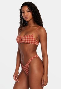 Červeno-biele kárované bikiny, ktoré obsahujú top s tenkými ramienkami a vysokými bikiny dnom, oboje vyrobené z hladkej tkaniny.