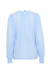 Vaaleansininen pusero, jossa pitkät, pussihihat, teksturoidut pilkut, takana napitus ja resorilla kiristettävät hihansuut. Malli on väljähkö.