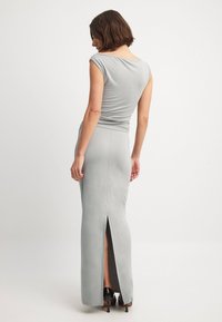 Graues, tailliertes Maxikleid mit kurzen Ärmeln, einem runden Ausschnitt und seitlichem Schlitz, aus glattem Stoff. Hochhackige Schuhe unterstreichen den Look.