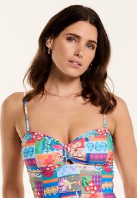 Spalvinga raštuota bikini liemenėlė su širdies formos iškirpte, reguliuojamomis petnešėlėmis ir dekoratyvine mazgo detalę centre. Pagaminta iš tamprios medžiagos.