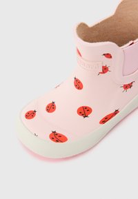 Botte de pluie pour enfants rose clair avec des motifs de coccinelles rouges et noires et une semelle texturée blanche.