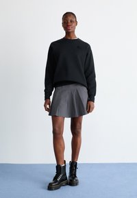 Sudadera negra, falda gris con pliegues y botas de combate negras con acentos amarillos. Textura suave, diseño casual, ajustada en la cintura, silueta suelta.
