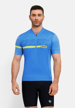 Mann trägt blaues kurzärmeliges Radsporttrikot mit gelbem Streifen und schwarze Radhosen, steht vor einfarbigem Hintergrund.
