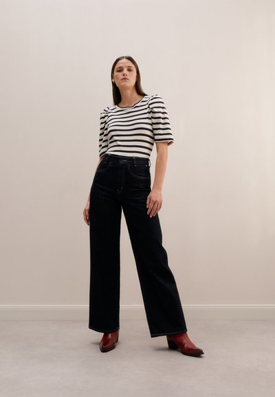 Striped black and white top with short puff sleeves, paired with high-waisted dark denim wide-leg pants and burgundy block-heeled boots.