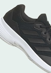 Sneaker sportivo nero con tomaia in tessuto strutturato, tre strisce nere e suola in gomma bianca con una leggera curva.