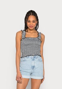 Top cropped em xadrez preto e branco com alças e barra franzidas, combinado com calções de ganga azul claro, com punhos dobrados.