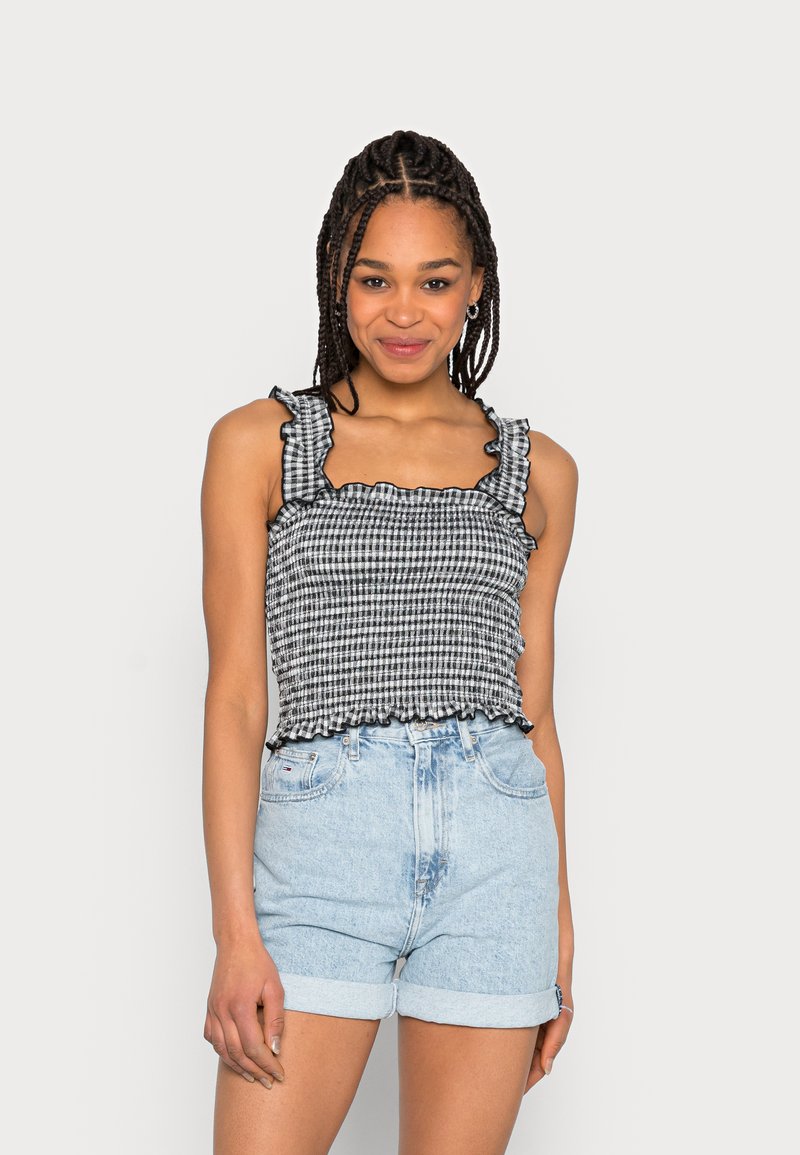 Top cropped em xadrez preto e branco com alças e barra franzidas, combinado com calções de ganga azul claro, com punhos dobrados.