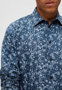 Mörkblå skjorta med knappar som har ett blommönster i ljusare nyanser. Tillverkad av ett strukturerat tyg med klassisk krage och svarta knappar.