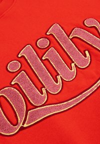 Rode sweatshirt met een grote, getextureerde grafiek in roze met een gele rand, die een zachte stof en gedurfde typografie toont.