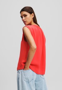 Blusa sin mangas roja con una textura suave, escote redondo y un corte ligeramente holgado, combinada con unos jeans de corte suelto en azul claro.