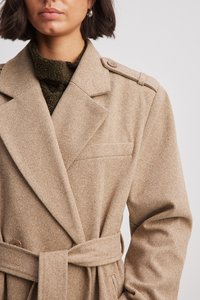 Beige trenčkot s vzorem rybí kost, vyrobený z texturované látky, s páskem v pase, velkými klopami a knoflíkovými akcenty na rameni.